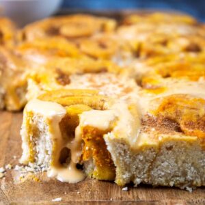 A close-up of a freshly baked cinnamon roll slab topped with gooey icing. The rolls are arranged closely on a wooden board, and the icing is melting over the edges, creating a warm and inviting appearance.