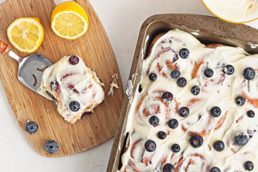 Lemon blueberry rolls in a pan with a slice on a cutting board.