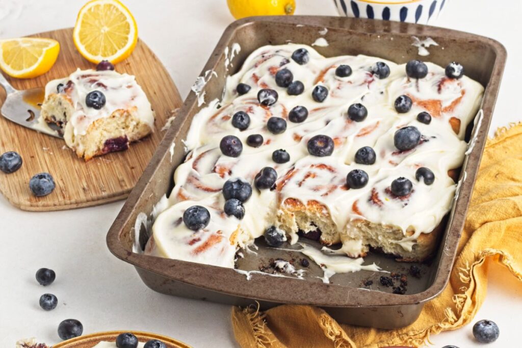 Lemon blueberry rolls in a pan with a slice on a cutting board.