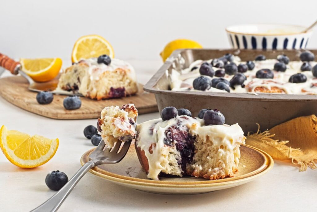 Lemon blueberry rolls in a pan with a slice on a cutting board with a fork.