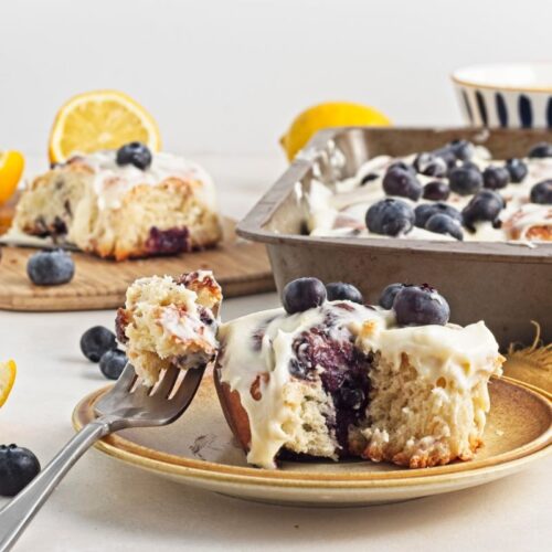 Lemon blueberry rolls in a pan with a slice on a cutting board with a fork.