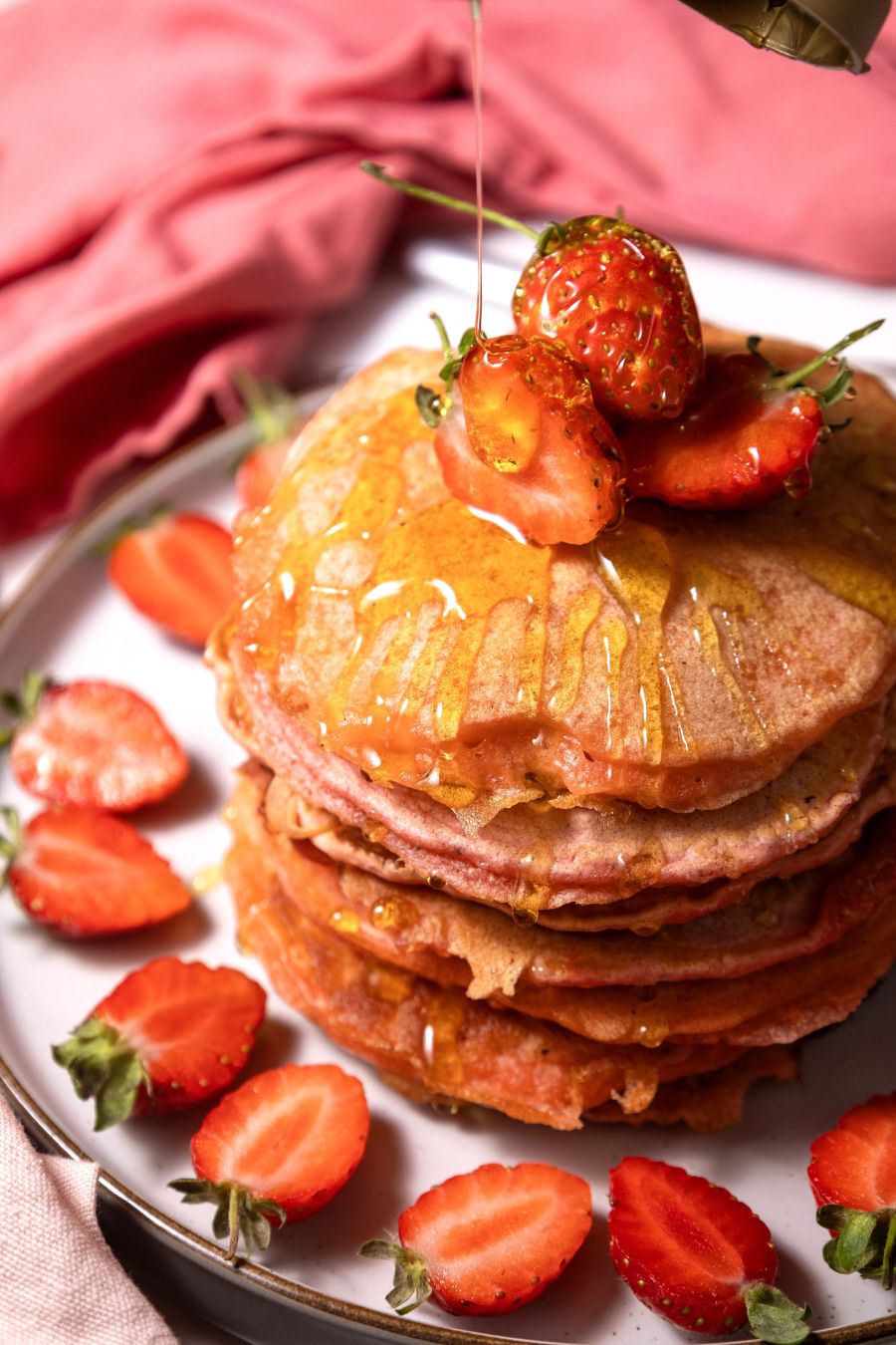 A stack of pancakes topped with sliced strawberries, surrounded by more strawberries on a plate.