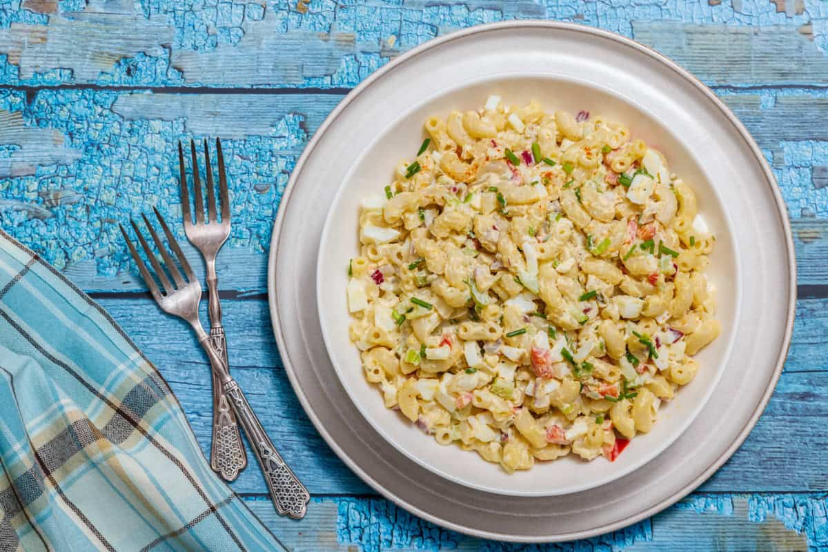 Plate of Deviled Egg Pasta Salad on a wooden table, accompanied by three forks and a blue plaid napkin.