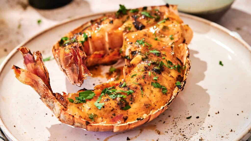 Grilled lobster tail served on a white plate, garnished with chopped herbs and black pepper.