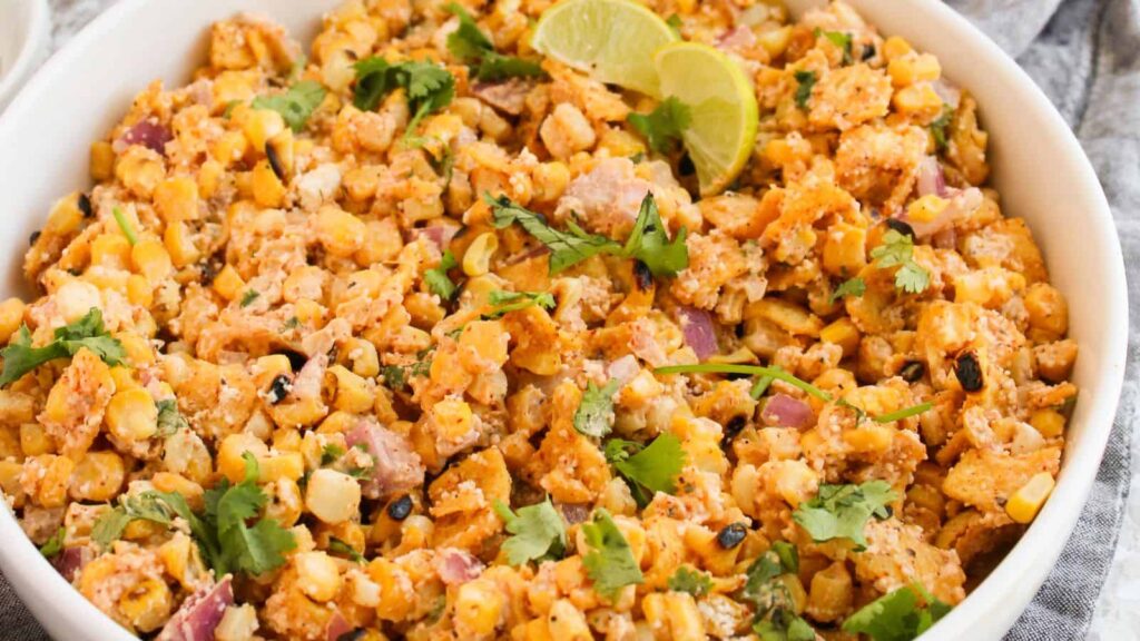 A bowl filled with Mexican street corn salad, garnished with cilantro and lime wedges—a true cool salads champ.