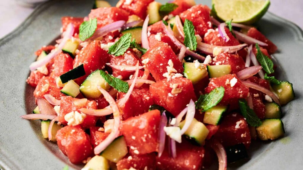 A plate of watermelon salad with diced watermelon, cucumber, red onion, feta cheese, mint leaves, and a lime wedge—one of the perfect salads for lazy weeknights.