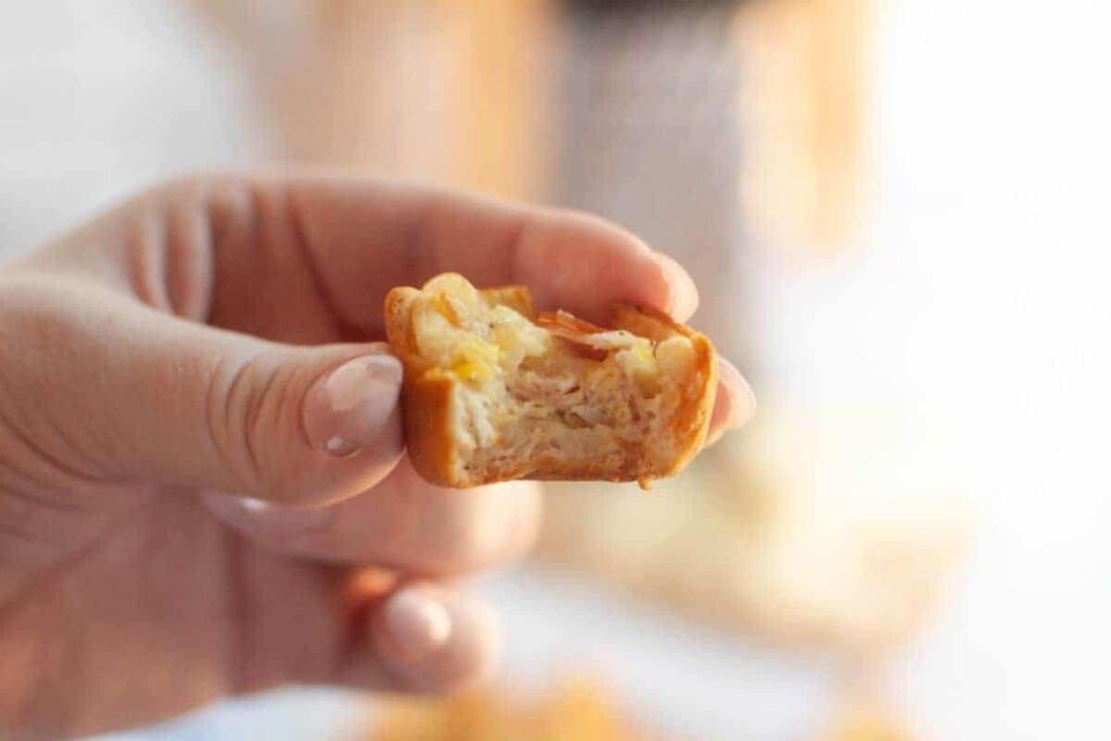 A hand holds a partially eaten Ham and Cheese puff, revealing layers of pastry, ham, and cheese.