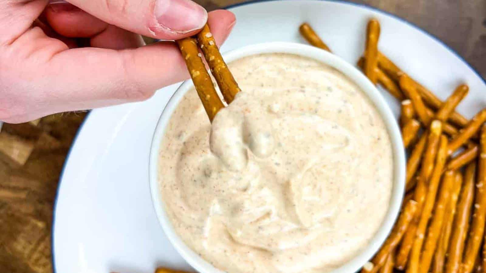 A person dipping a pretzel into a bowl of cajun dip.