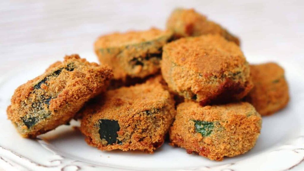 A close-up of several golden-brown breaded and fried zucchini slices on a white plate.