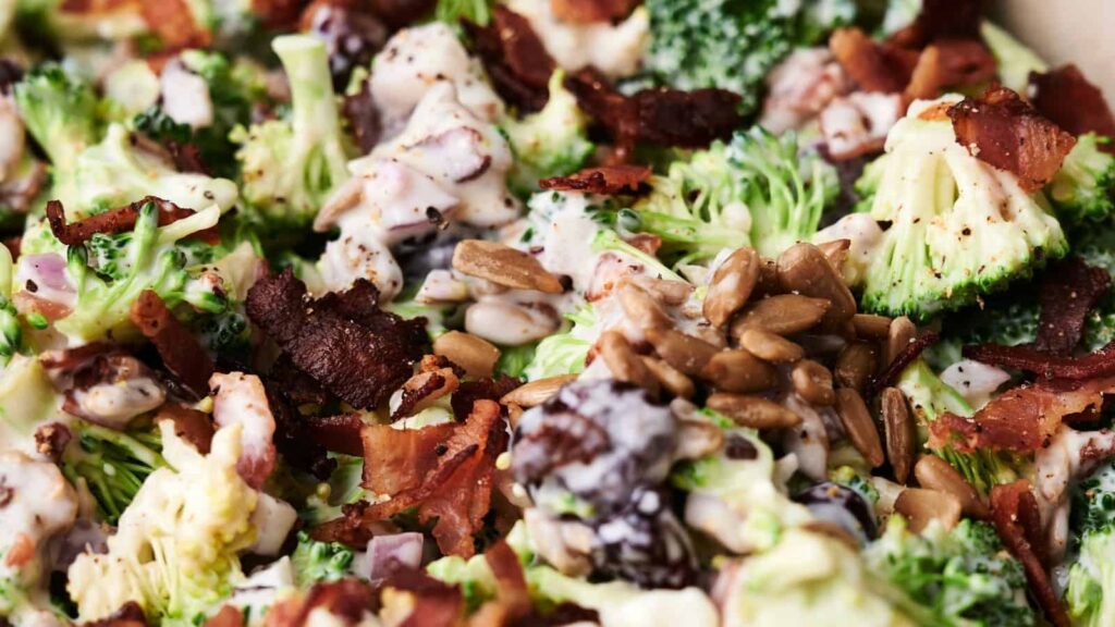 A close-up of a broccoli salad with bacon, sunflower seeds, and a creamy dressing.