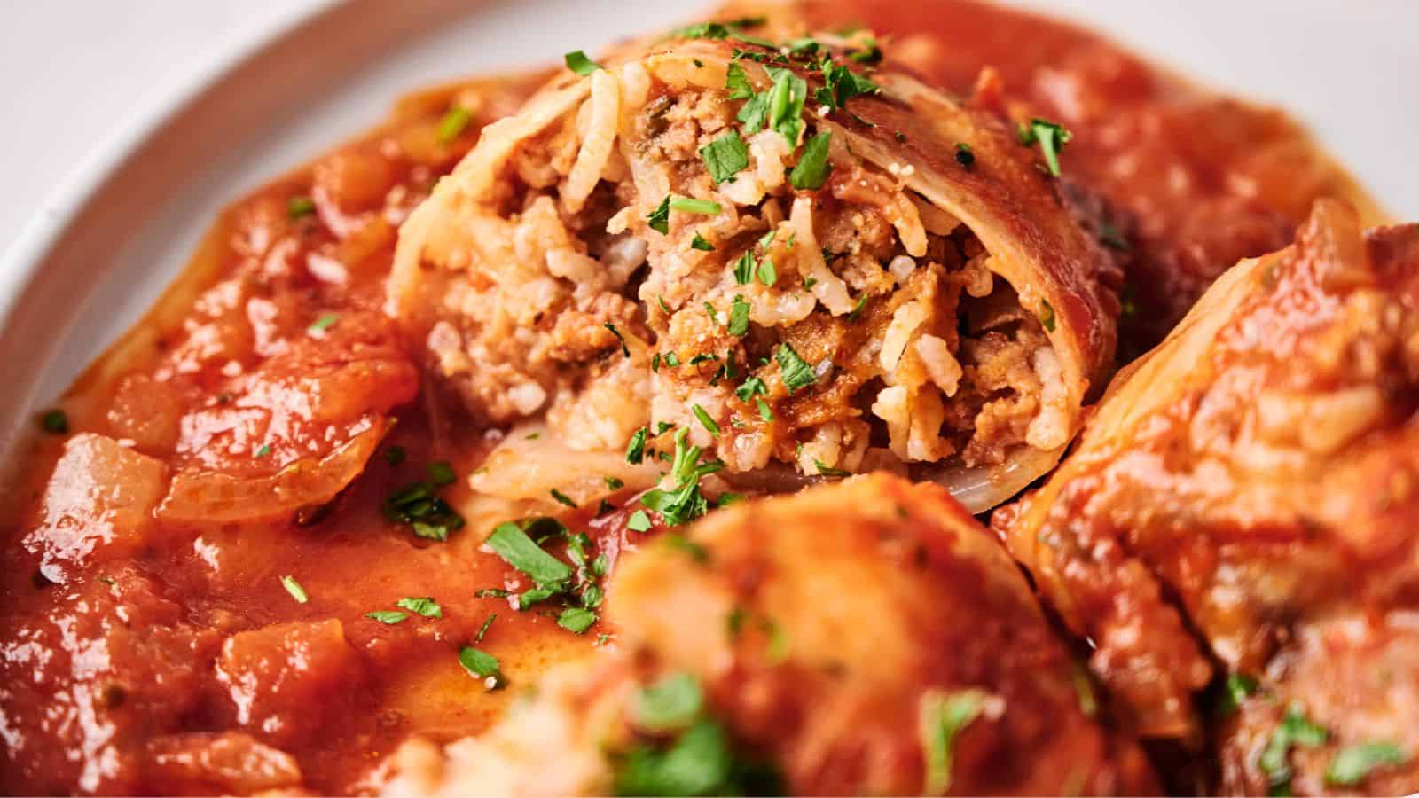 Close-up of stuffed cabbage rolls filled with rice and ground meat, topped with tomato sauce and garnished with chopped herbs.