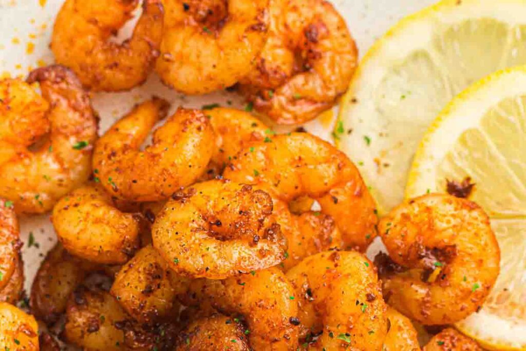 Seasoned cooked shrimp arranged beside slices of fresh lemon on a light surface.