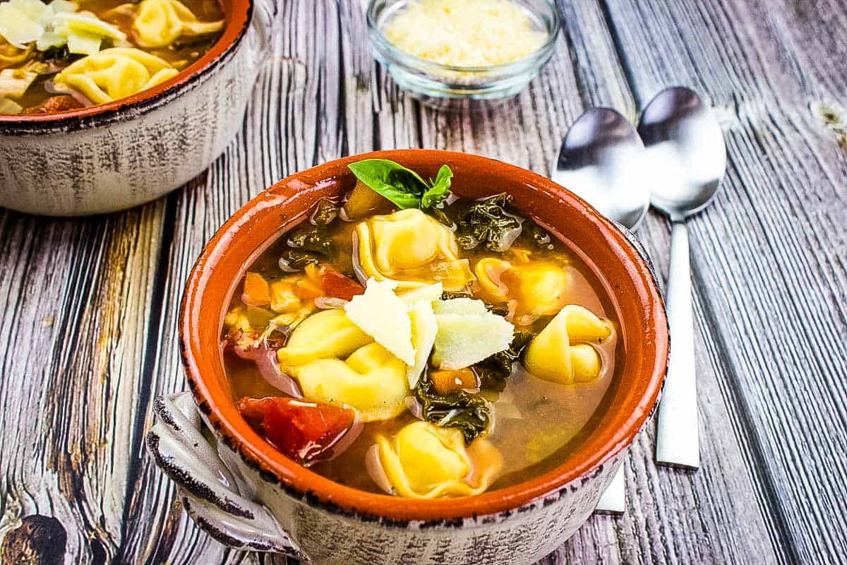 Tortellini Soup with Kale & Chicken in a bowl on a wooden table.