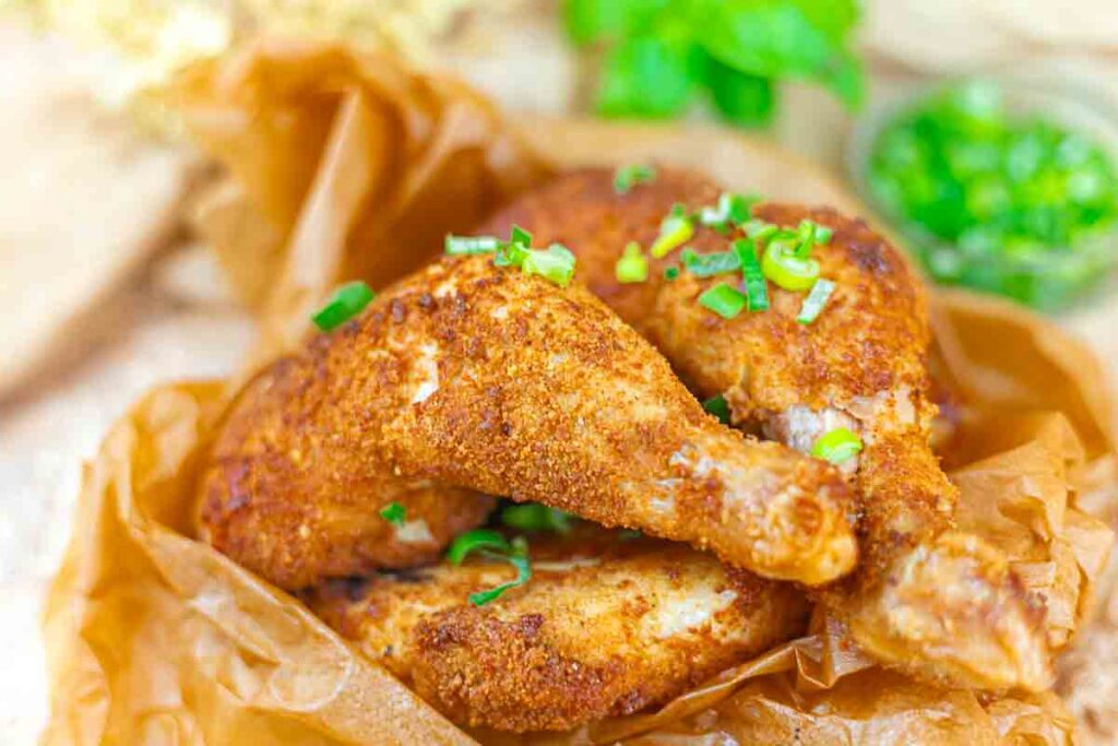 Two pieces of seasoned, breaded fried chicken garnished with chopped green onions on brown parchment paper.