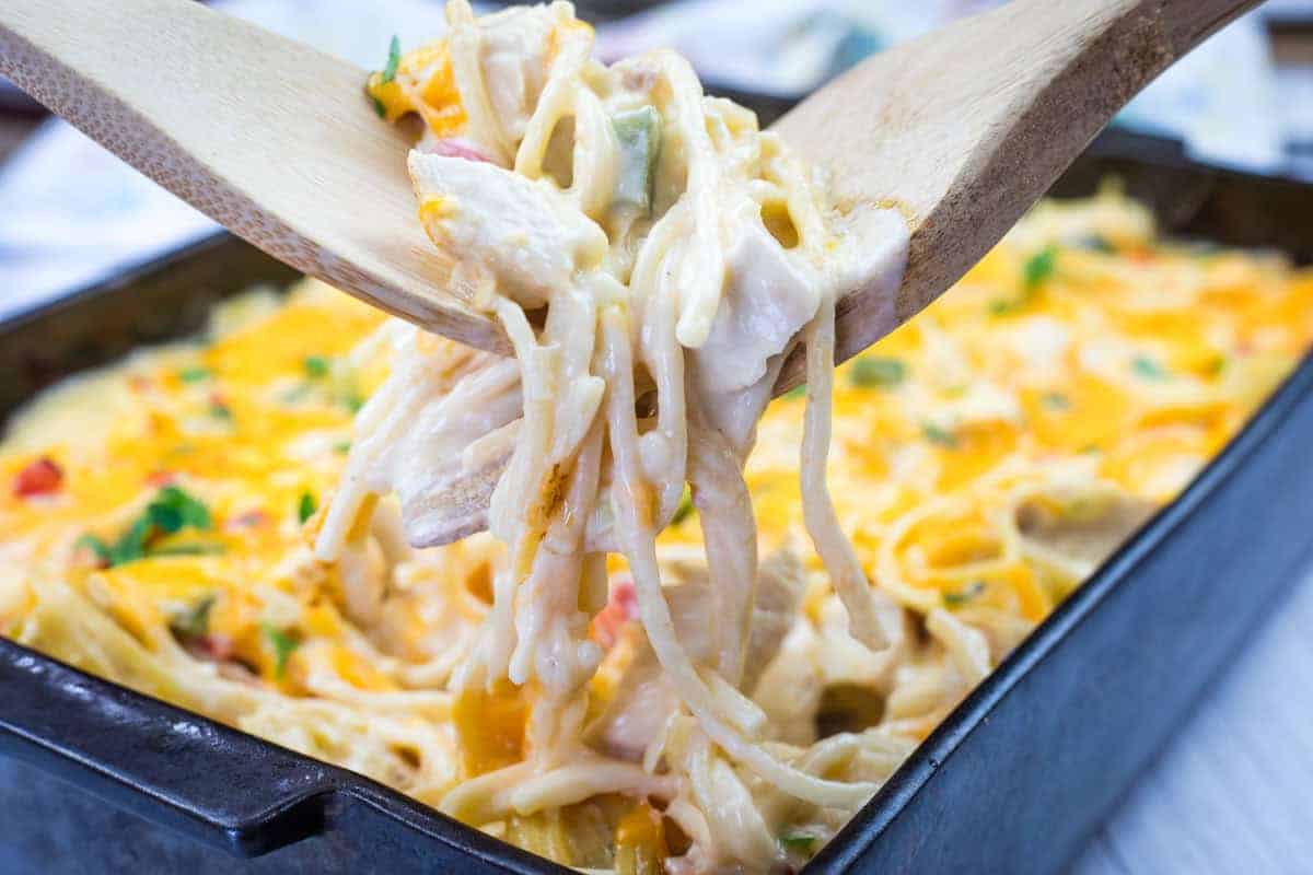 Wooden utensils lifting chicken spaghetti from a baking dish.