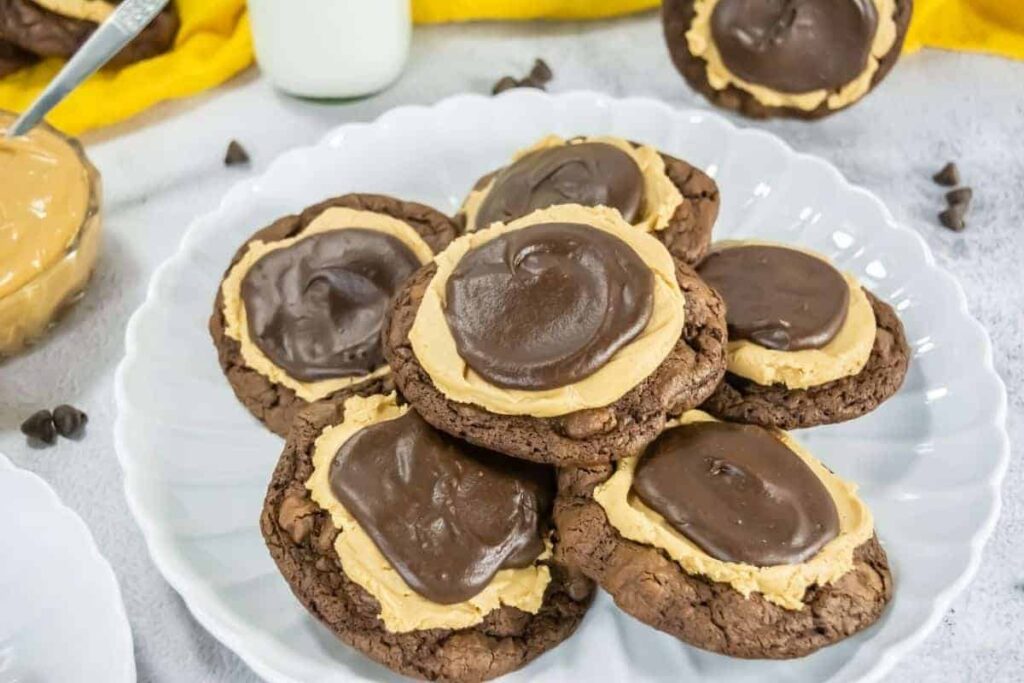 A plate with several Crumbl Copycat Buckeye Brownie cookies topped with a layer of peanut butter and a swirl of chocolate frosting.