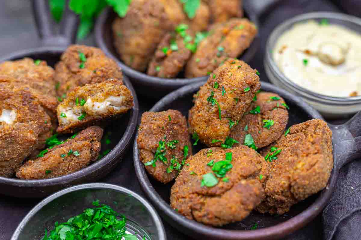 Three bowls filled with golden-brown chicken nuggets garnished with chopped parsley, served with a small bowl of creamy dipping sauce.