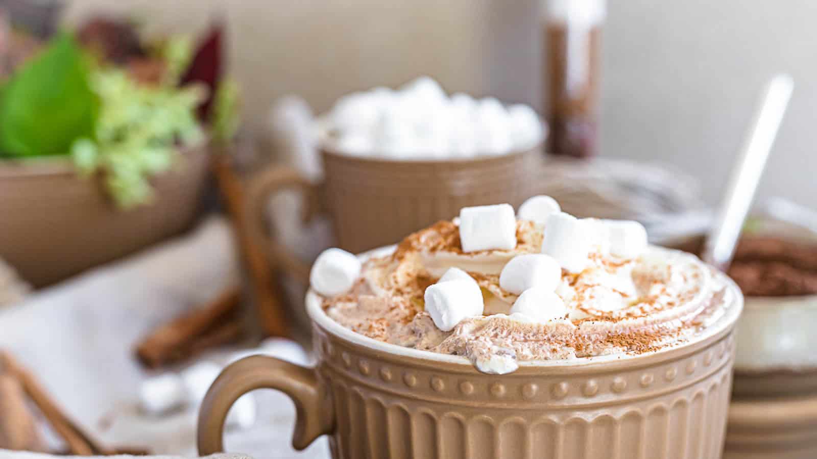 A glass mug of hot chocolate topped with whipped cream, mini marshmallows, and chocolate chips.