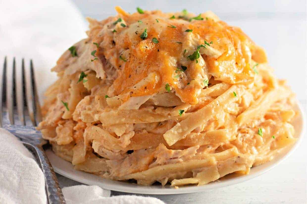 A plate of Chicken Tetrazzini topped with melted cheese and sprinkled with chopped herbs, with a fork and napkin beside it.
