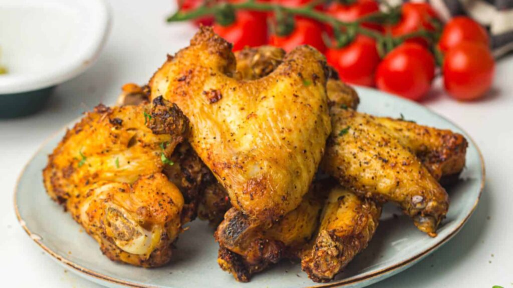 Roasted chicken wings on a plate with a side of cherry tomatoes.