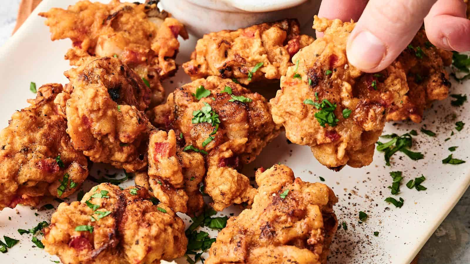 A plate of golden-brown fritters garnished with chopped herbs, served with a dipping sauce and a wedge of lemon.