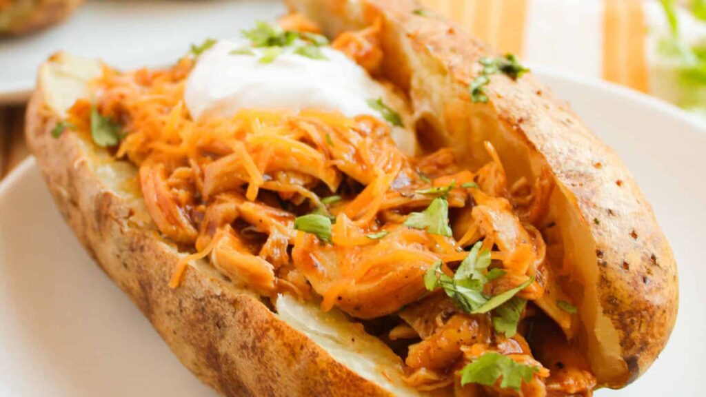 Baked potato topped with shredded barbecue chicken, cheese, sour cream, and garnished with parsley.