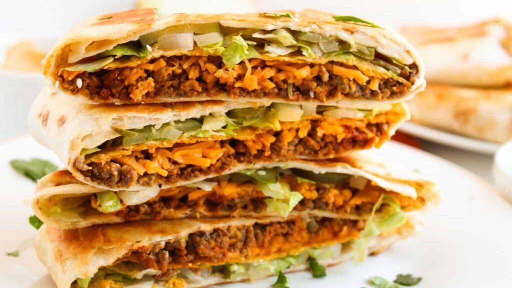 Three folded wraps are stacked, showing layers of ground beef, melted cheese, lettuce, and other fillings.