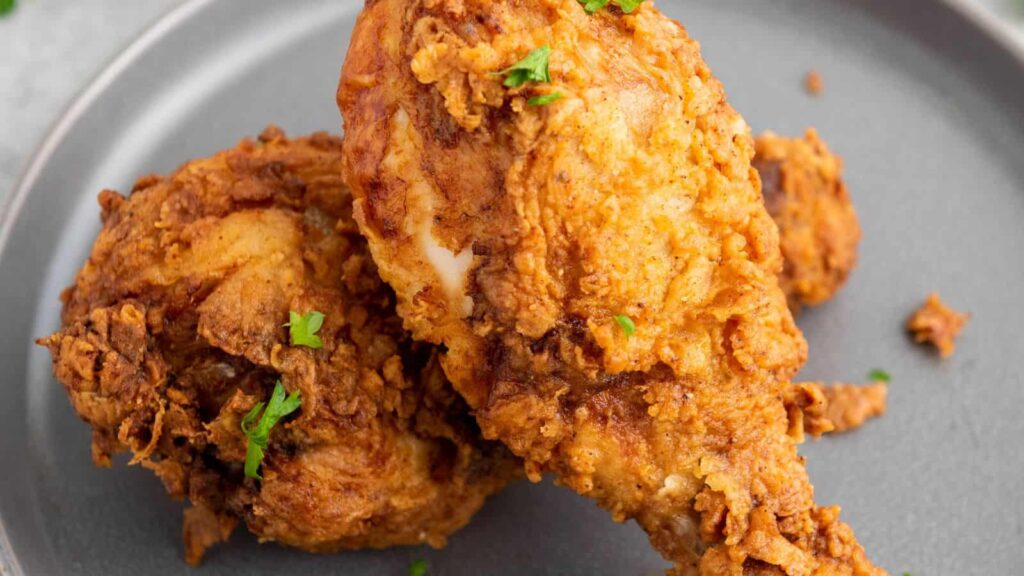 Two pieces of crispy fried chicken garnished with fresh parsley on a gray plate.
