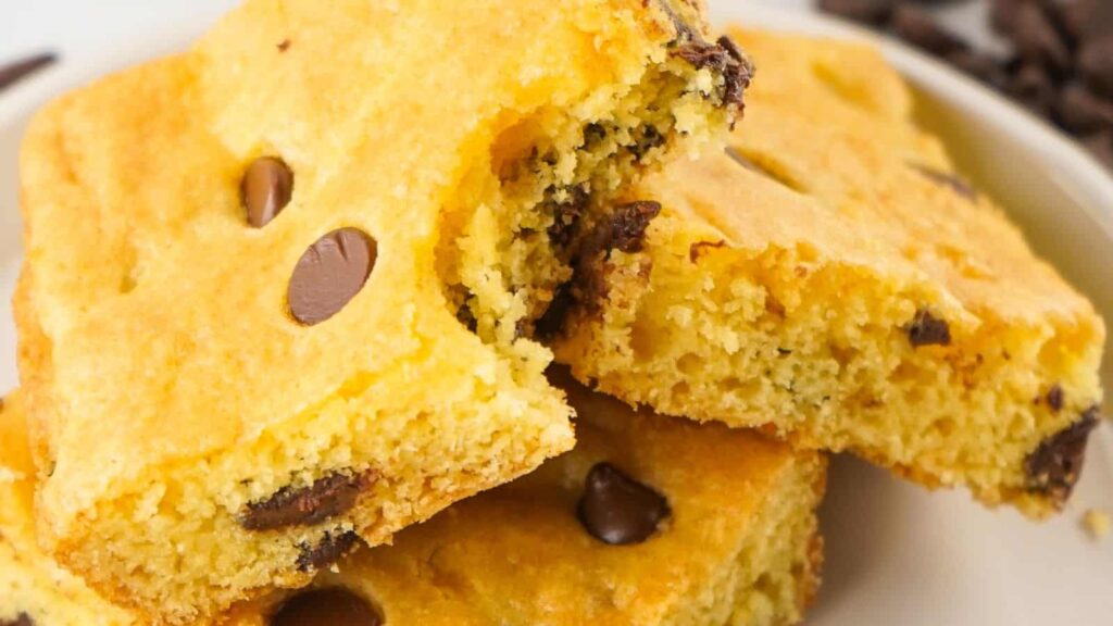 A close-up of a stack of chocolate chip blondies, with a bite taken out of one.