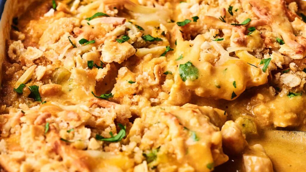 Close-up of a creamy dish featuring baked chicken topped with a golden-brown crumb crust, garnished with chopped parsley. The sauce is thick, with visible chunks and shredded cheese.