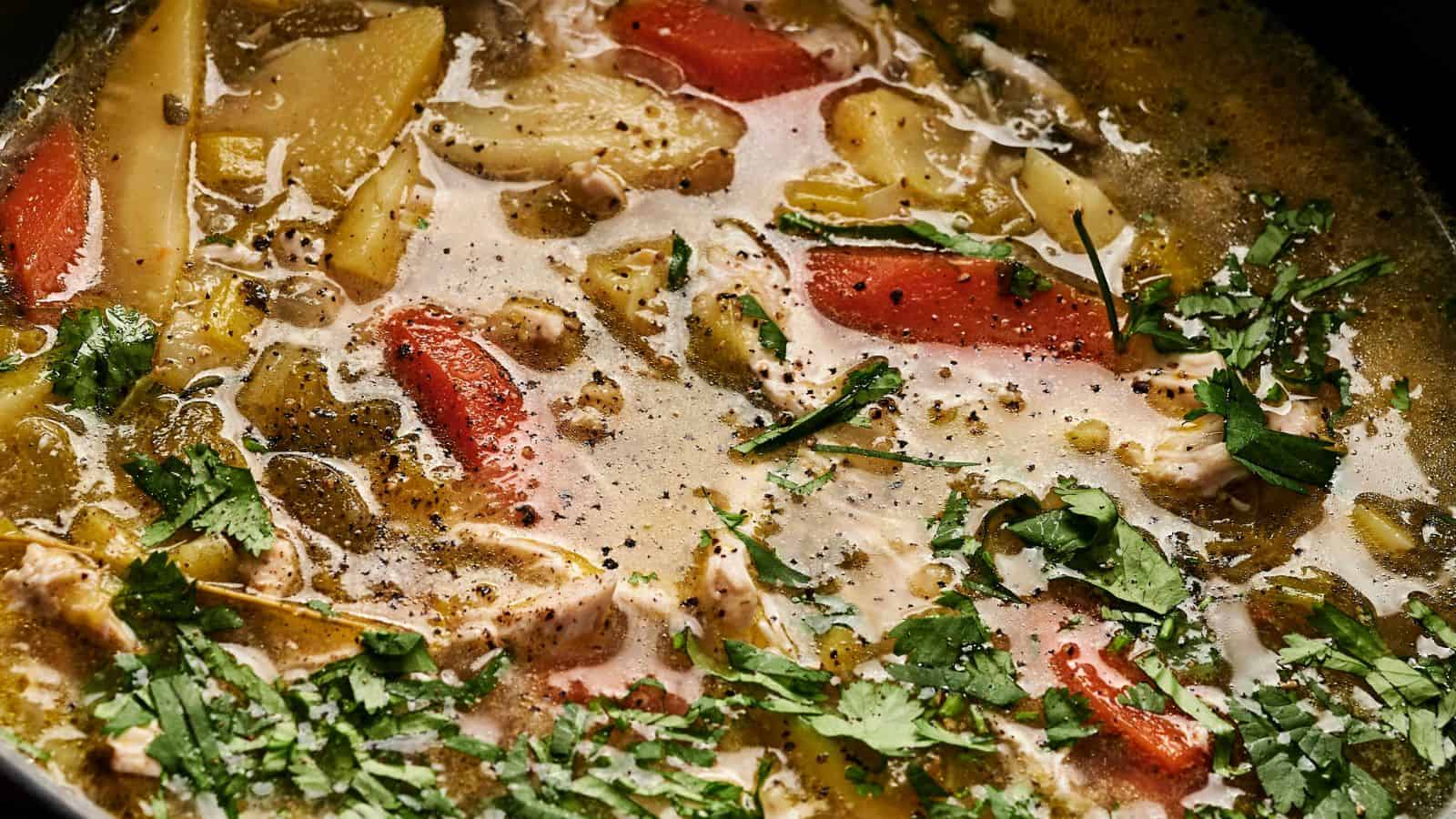 A pot of soup with sliced carrots, potatoes, and herbs floating in a seasoned broth.