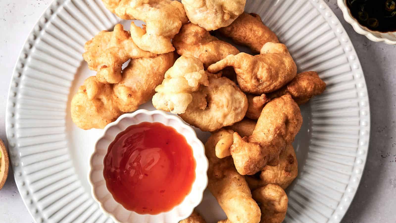 Plate of batter-fried fritters with a bowl of red dipping sauce on a white plate, viewed from above.