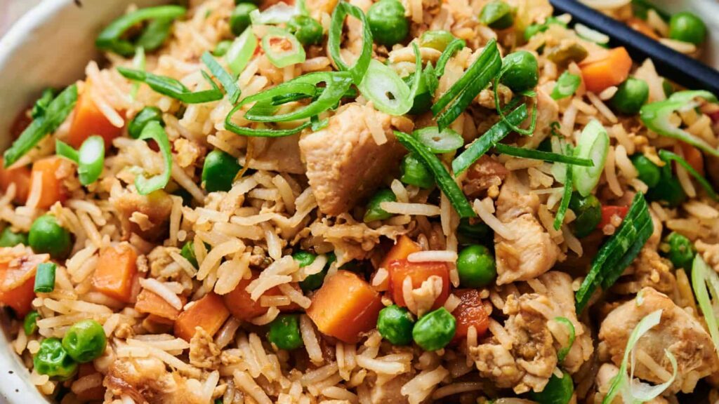 A close-up of chicken fried rice garnished with sliced green onions. The dish includes peas, carrots, and seasoned white rice.