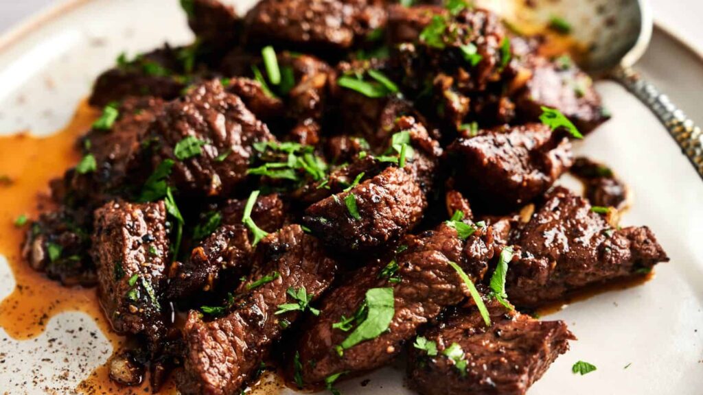 Plate of cooked beef chunks garnished with chopped fresh herbs, served with a bit of sauce on a light-colored dish.