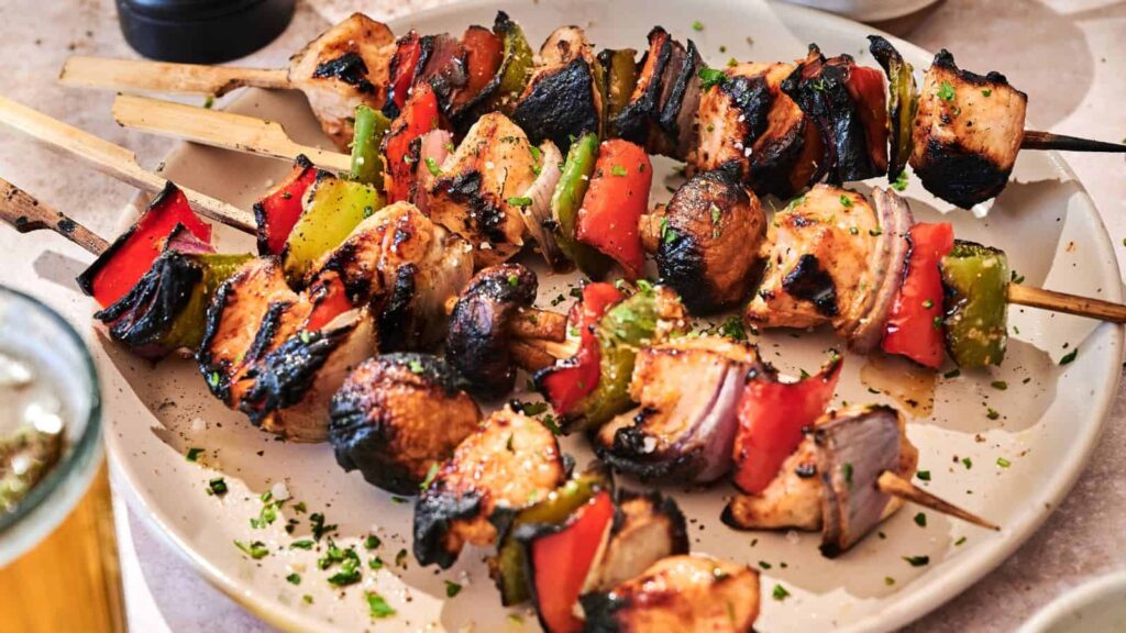 Grilled chicken skewers with red bell peppers, green bell peppers, and onions are served on a white plate, garnished with chopped herbs.