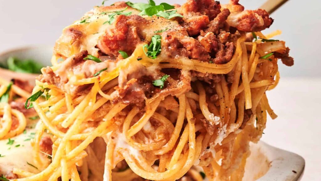 A serving of baked spaghetti with melted cheese and meat sauce, garnished with parsley.