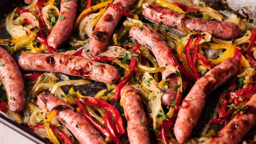 Sausages baked on a sheet pan with sliced red and yellow bell peppers and onions, garnished with chopped herbs.