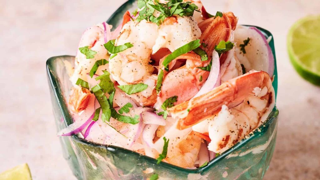 A close-up of shrimp ceviche with sliced red onions and chopped cilantro, served in a decorative green bowl.