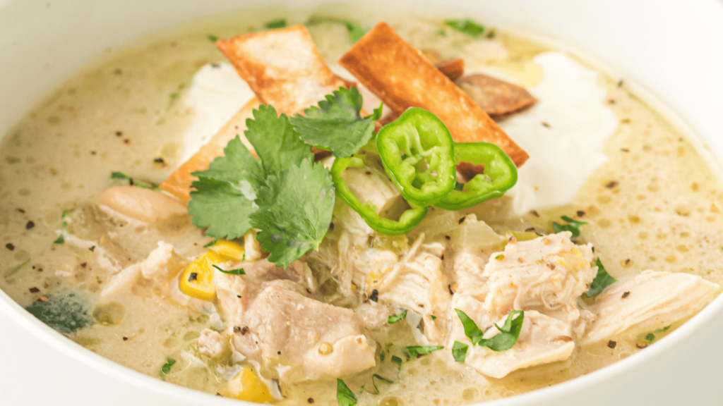 A bowl of creamy chicken soup topped with tortilla strips, sliced jalapeños, cilantro, and a dollop of sour cream.