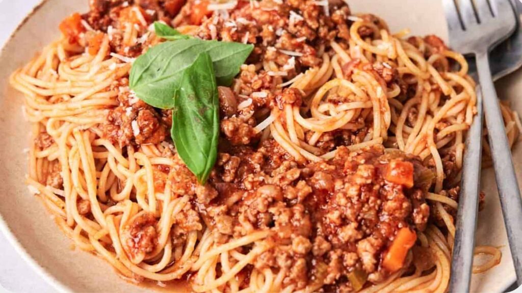 A plate of spaghetti topped with meat sauce and a basil leaf, served with a fork on the side.