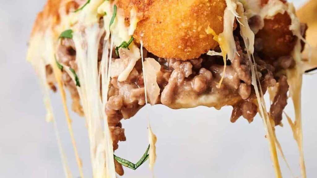 A cheesy bean and beef burrito being pulled apart, showing the melted cheese and fillings.