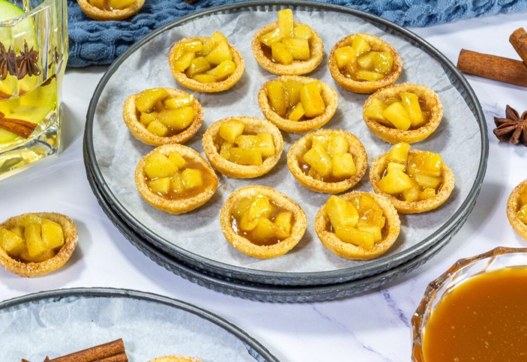 Mini caramel apple bites arranged on a parchment-lined plate with cinnamon sticks and star anise for a cozy dessert presentation.