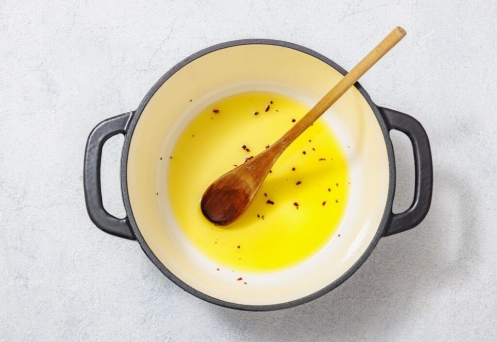 A cast iron skillet with olive oil and chili flakes, with a wooden spoon resting in it. The oil is heated and ready for cooking.