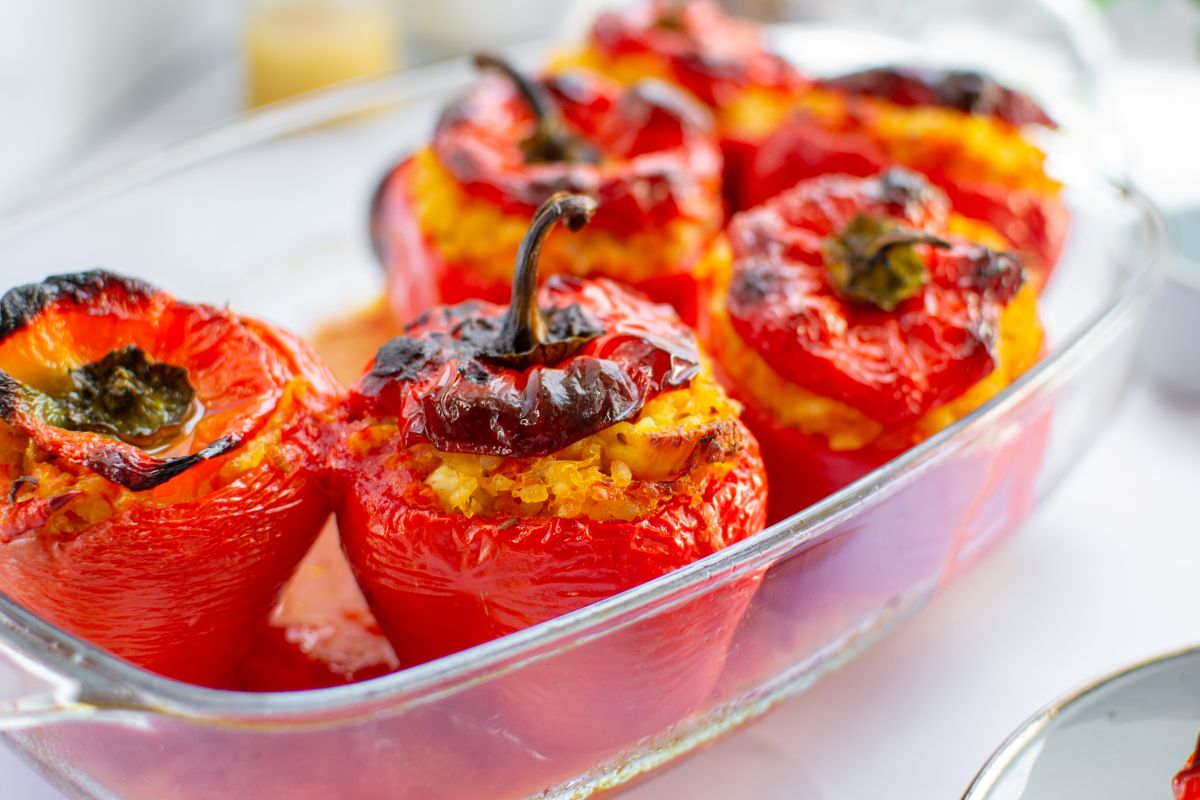 A glass baking dish filled with roasted red bell peppers stuffed with a yellow rice mixture, with charred tops, sitting on a white surface.
