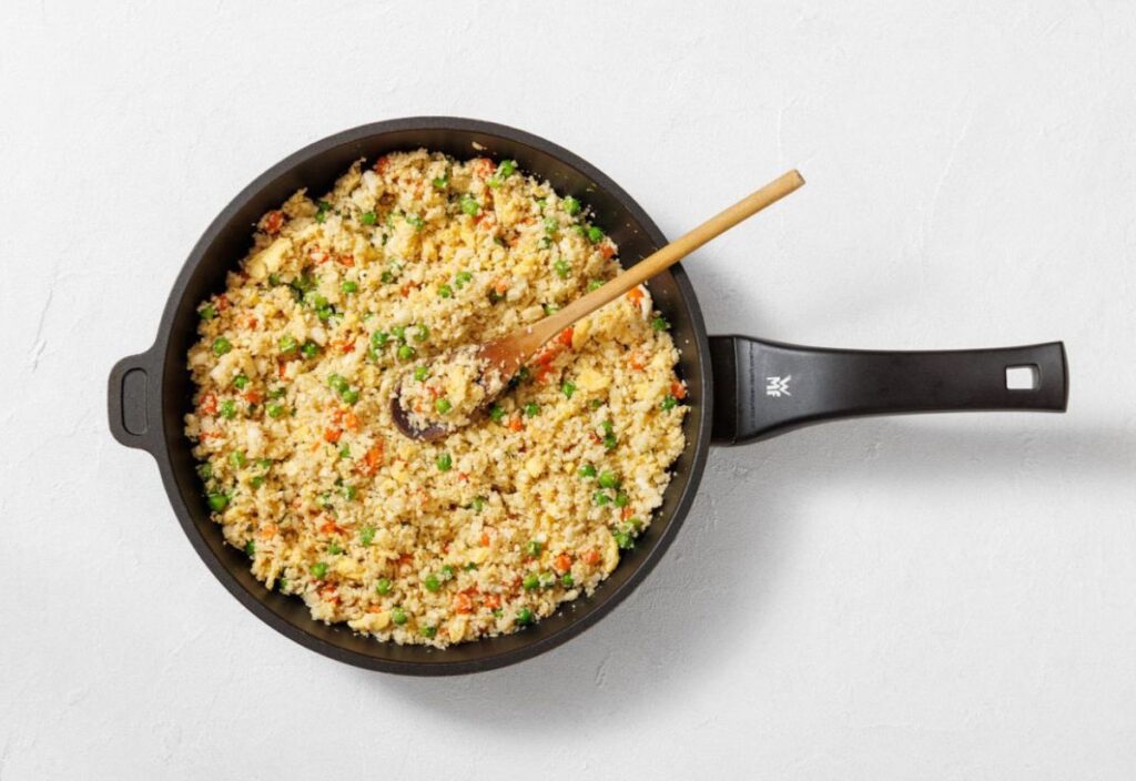 A finished cauliflower fried rice in a skillet, garnished with vegetables.