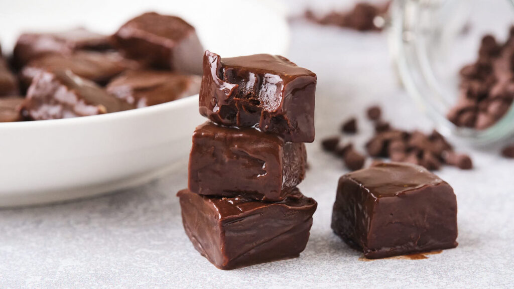 Blocks of chewy fudge are stacked on top of each other on a light colored surface.
