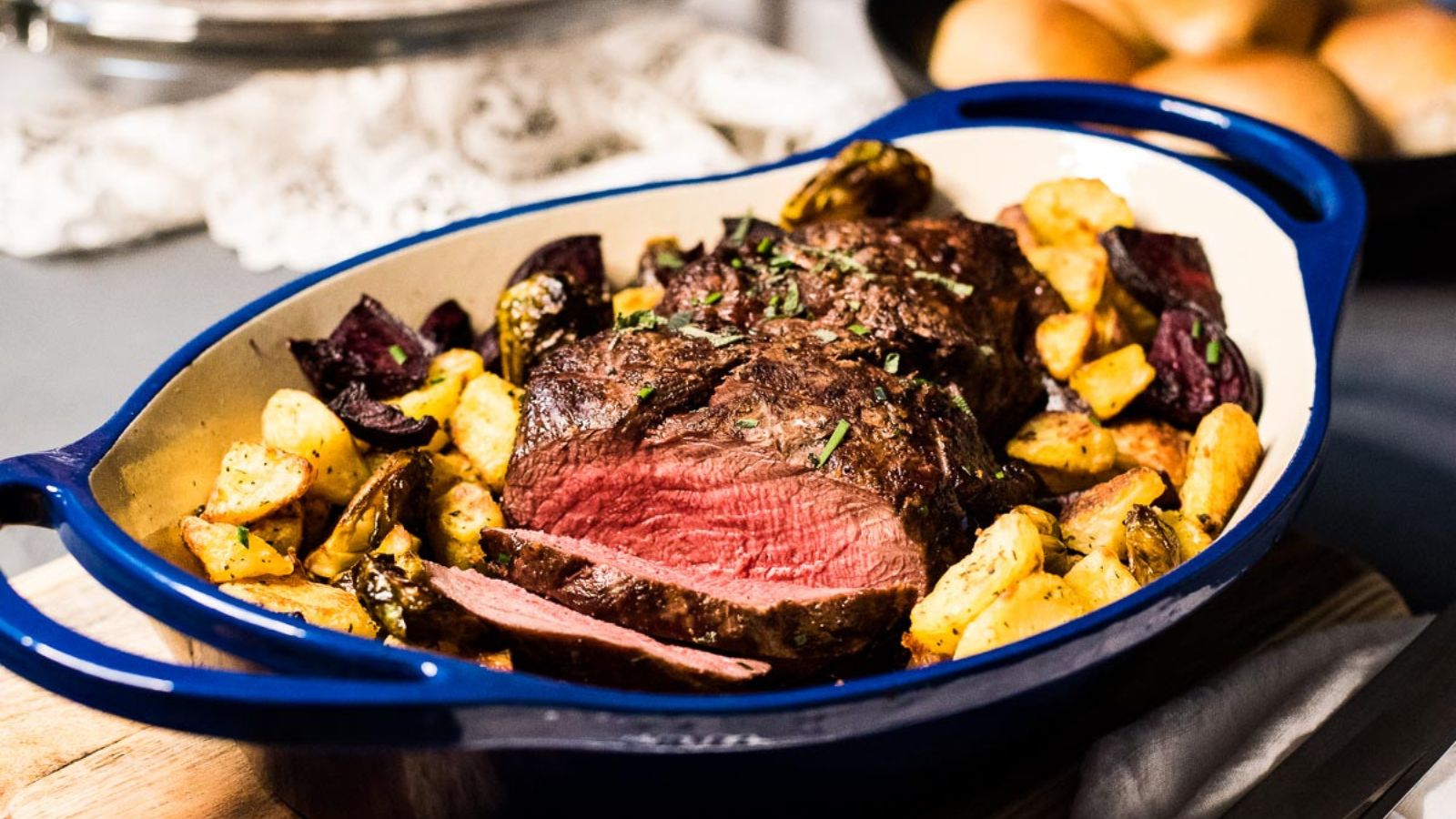 Blue roasting dish with beef roast, red center, and roasted potatoes and vegetables.