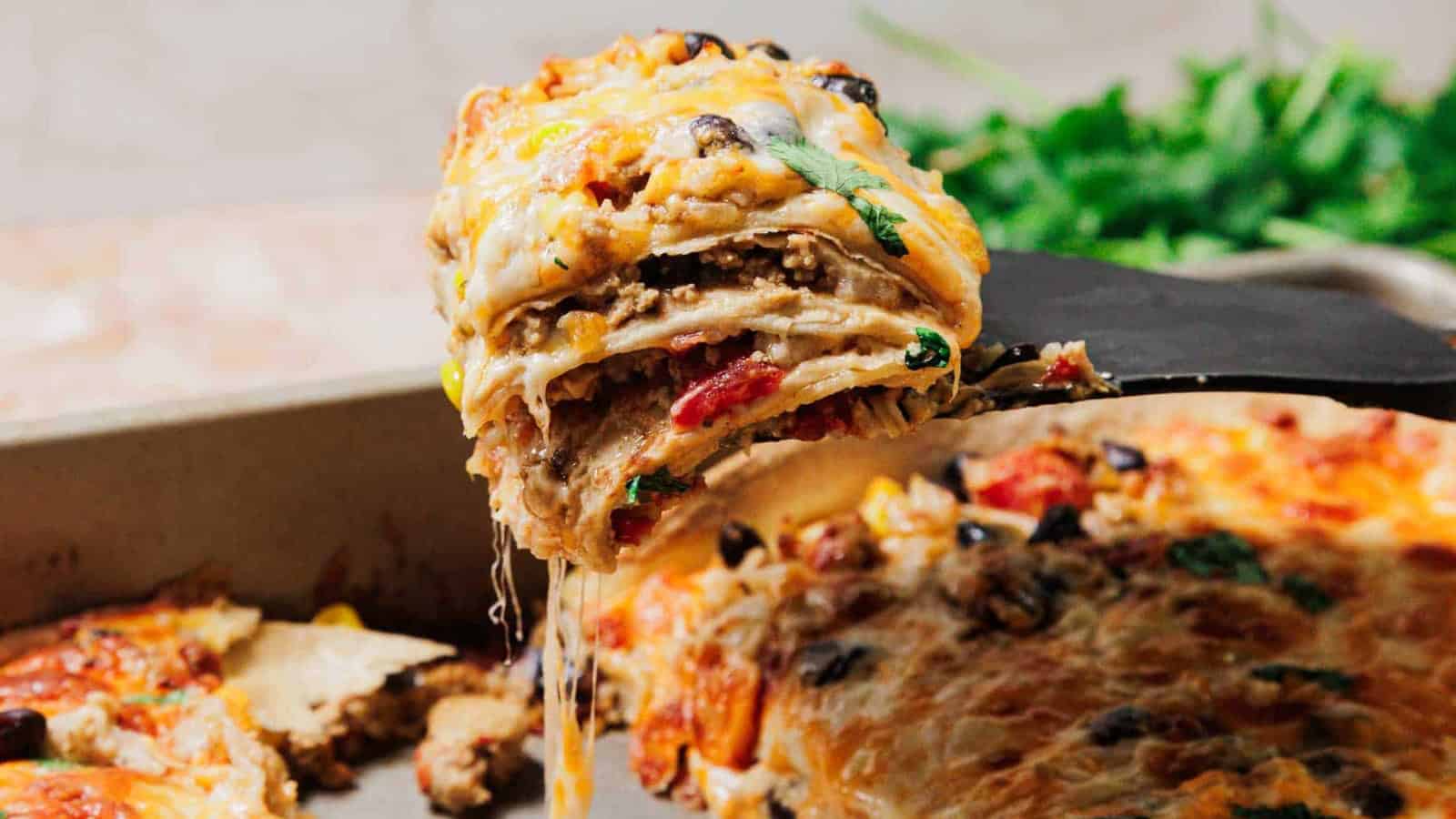 A cheesy slice of layered Mexican casserole being lifted from a baking dish, with melted cheese stretching.