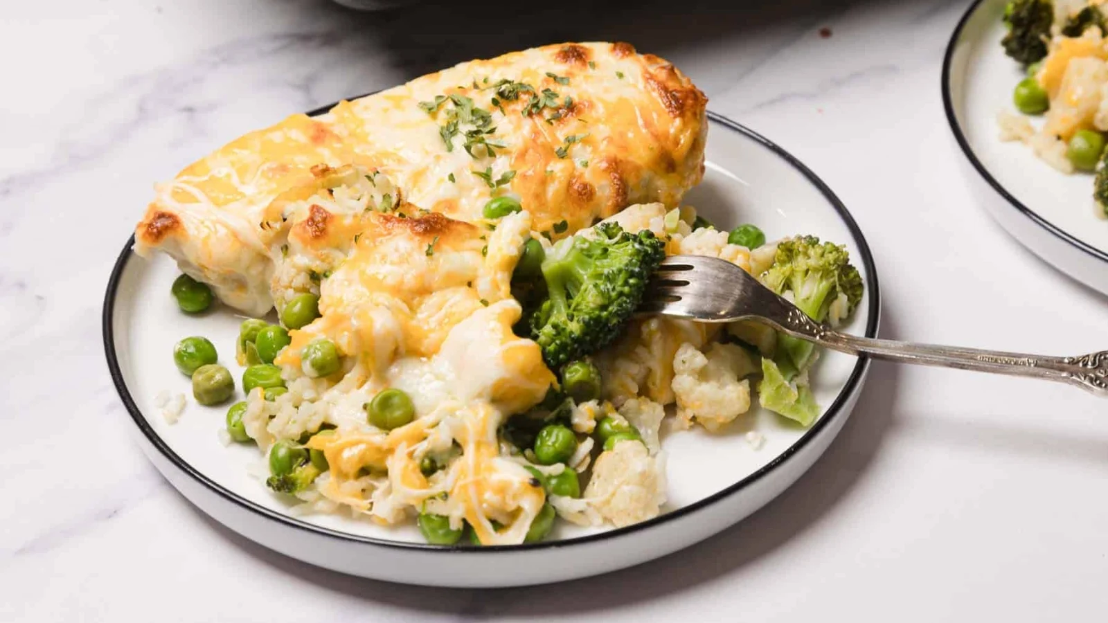 A plate of cheesy vegetable casserole with broccoli, peas, and cauliflower, with a fork lifting a bite.