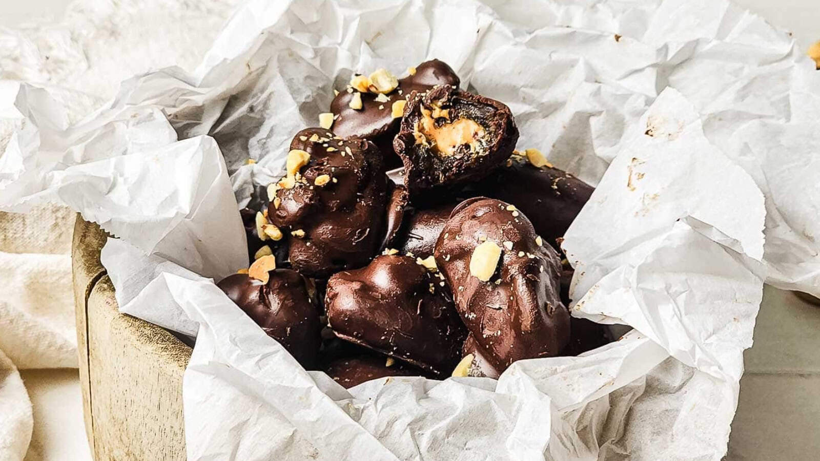 Chocolate-covered candies with a peanut butter filling, topped with crushed nuts, in a box lined with parchment paper.